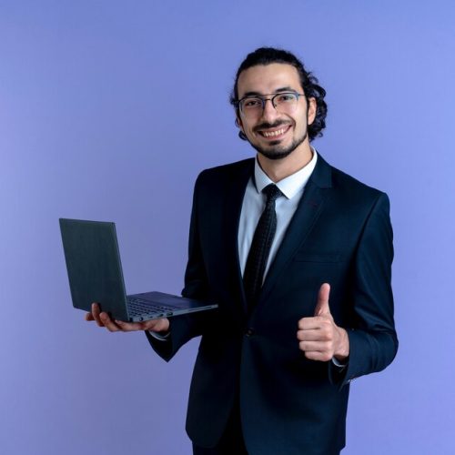 homme-affaires-costume-noir-lunettes-tenant-ordinateur-portable-avant-souriant-montrant-pouces-vers-haut-debout-mur-bleu_141793-50755 homme-affaires-costume-noir-lunettes-tenant-ordinateur-portable-avant-souriant-montrant-pouces-vers-haut-debout-mur-bleu_141793-50755